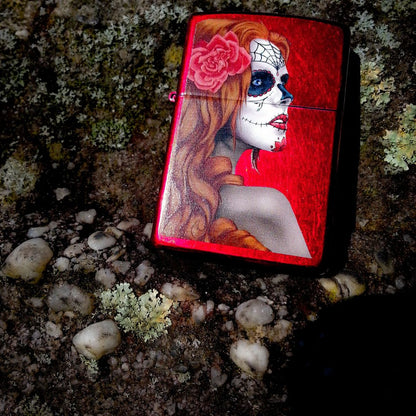 Lifestyle image of Day of the Dead: Girl Candy Apple Red Windproof Lighter laying on rocks showing the front of the lighter.

