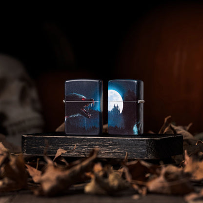 Lifestyle image of two Zippo Horror Wolf 540 Matte Windproof Lighters; one showing the front of the lighter while the other shows the back and hinge side of the lighter. They are both standing on a dark wooden block surrounded by brown leaves with a skull in the background. 

