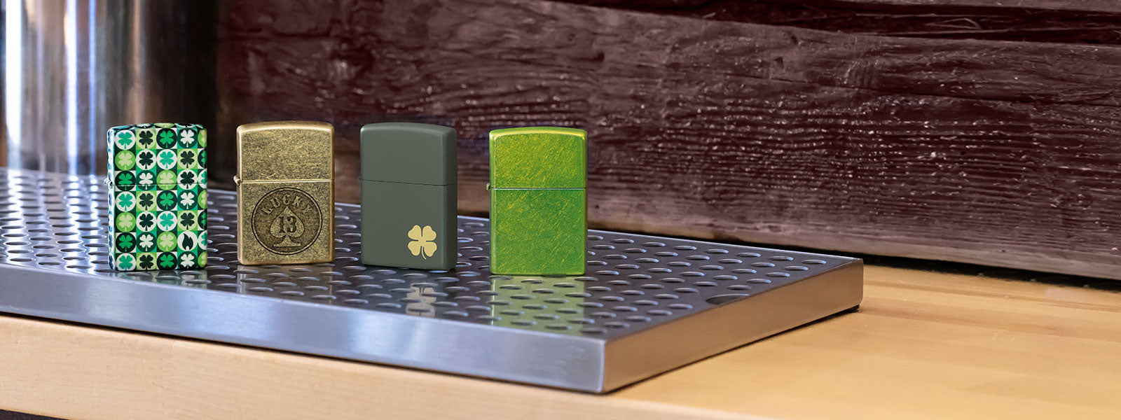 Four green and gold Zippo lighters on a metallic surface with a wooden background.