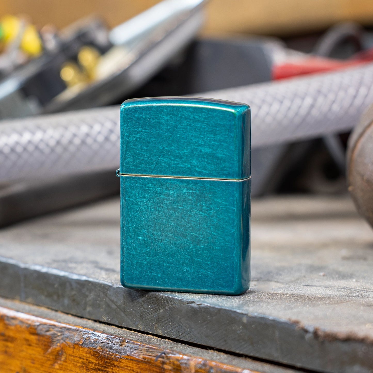 Lifestyle image of Zippo Classic Candy Teal Windproof Lighter standing on a workbench showing the front of the lighter. 

