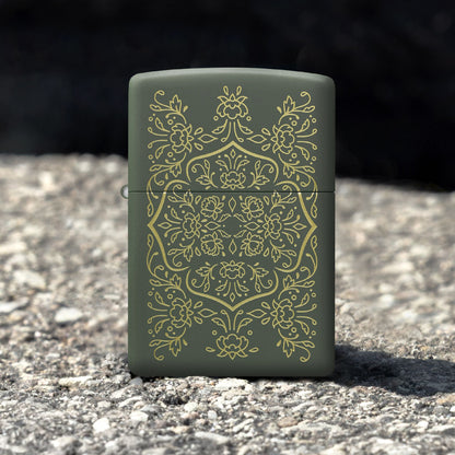 Lifestyle image of Zippo Floral Mandala Design Green Matte Windproof Lighter standing on an asphalt surface while showing the front of the lighter. 

