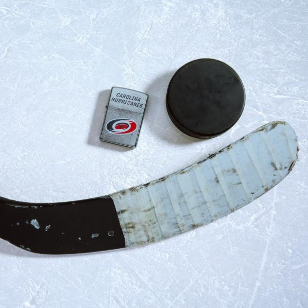 Lifestyle image of the NHL Anaheim Ducksr Street Chrome Windproof Lighter laying on ice with a hockey puck and stick