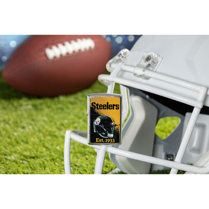 Lifestyle image of Zippo NFL Pittsburgh Steelers Helmet Design Street Chrome Windproof Lighter standing on the facemask of a white helmet showing the front of the lighter with a football lying on a football field as the background.

