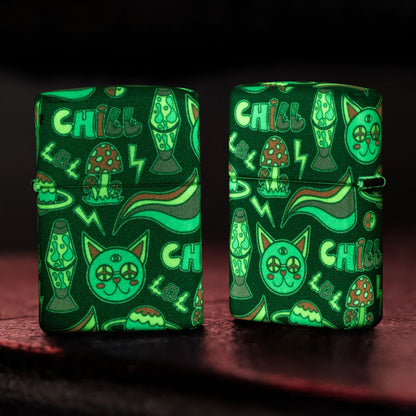 Lifestyle image of two Zippo Glowing Chill Design Glow-in-the-Dark Green Windproof Lighters standing on an old leather chest while glowing in the dark; one showing the front while the other is showing the back and hinge side of the lighter. 

