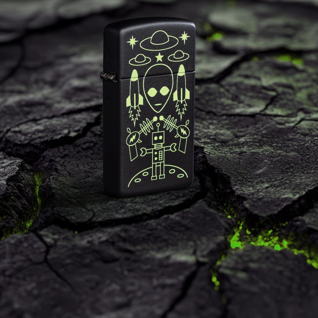 Lifestyle image of Zippo Alien Invasion Design Slim® Black Matte Windproof Lighter standing on blacktop with green glowing cracks.