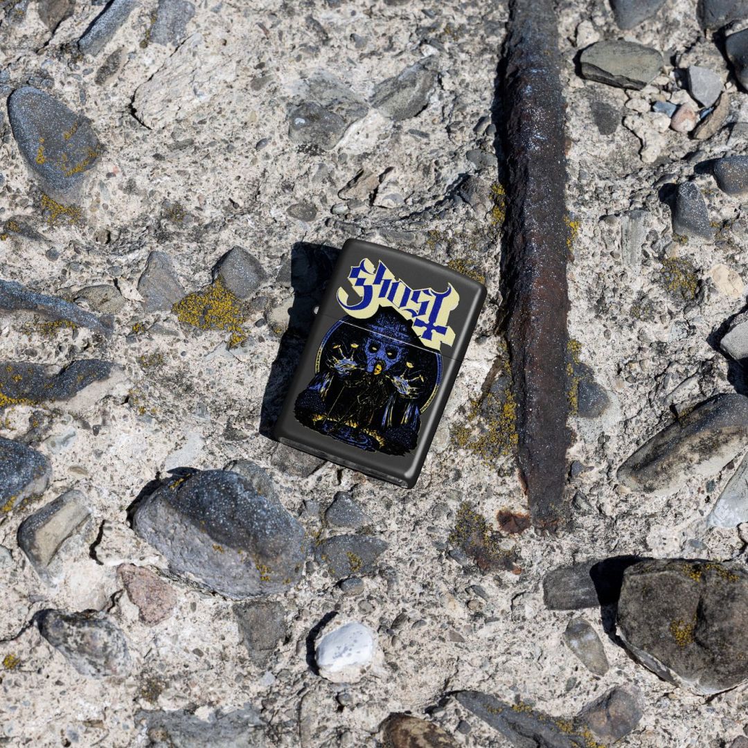 Lifestyle image of Zippo Ghost Papa Design Black Matte Windproof Lighter lying on a rocky surface showing the front of the lighter. 

