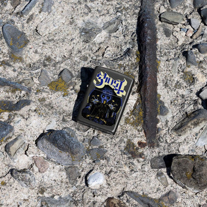 Lifestyle image of Zippo Ghost Papa Design Black Matte Windproof Lighter lying on a rocky surface showing the front of the lighter. 

