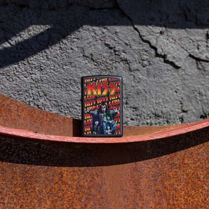 Lifestyle image of Zippo KISS® Poster Design Black Matte Windproof Lighter standing on a rusty surface showing the front of the lighter with a grey concrete wall as the background.

