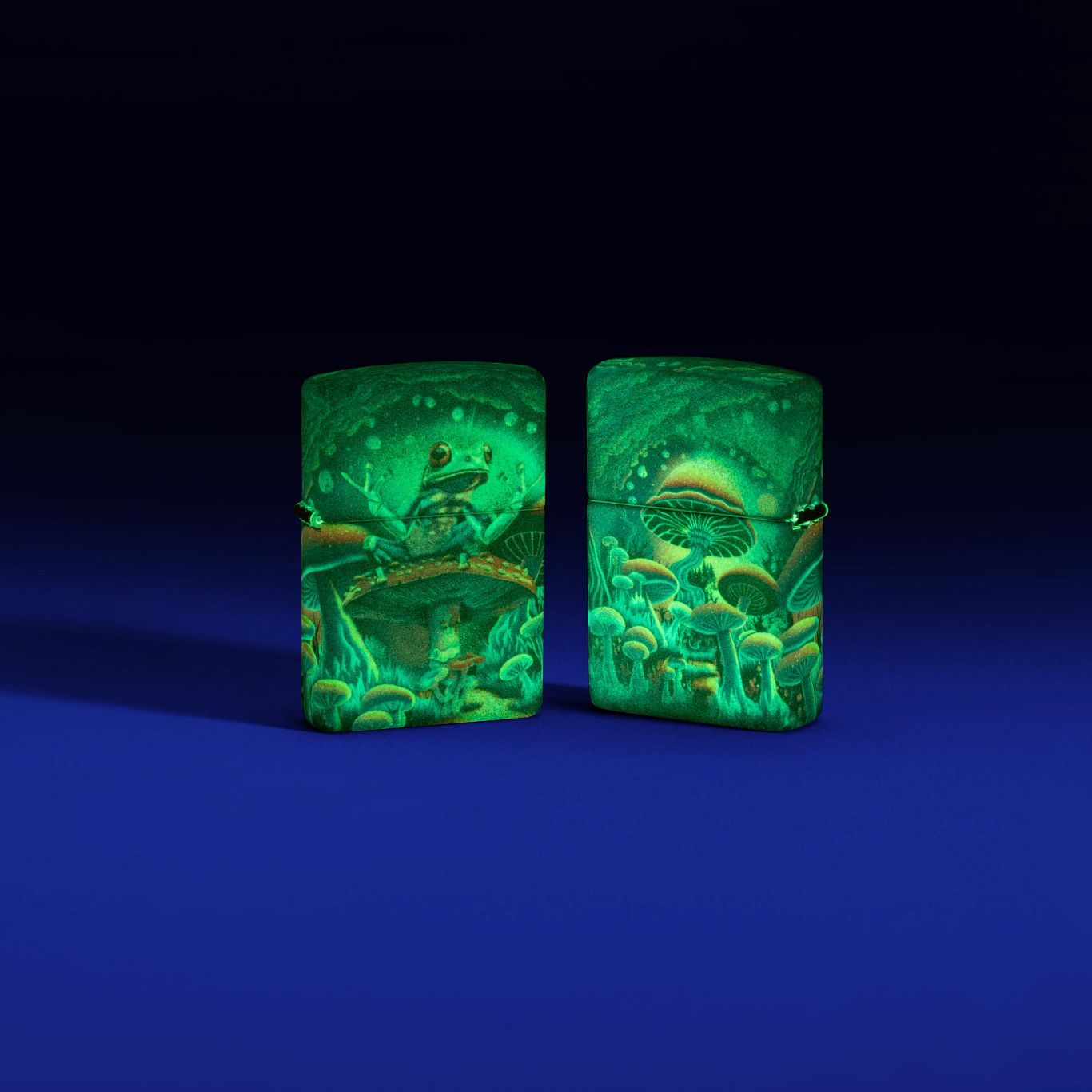 Lifestyle image of two Zippo Zen Frog Design Glow in the Dark Matte Windproof Lighters, one showing the front of the lighter and the other showing the back, glowing in the dark.