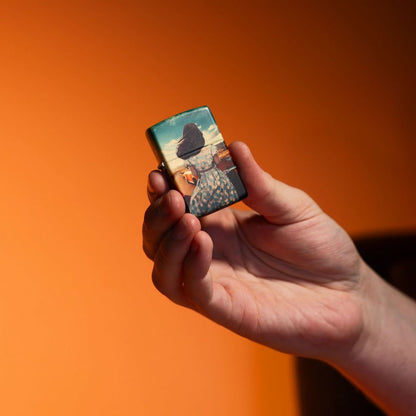 Lifestyle image of Zippo American Road Trip Design 540 Color Windproof Lighter closed in hand showing the front of the lighter with an orange ombre background. 

