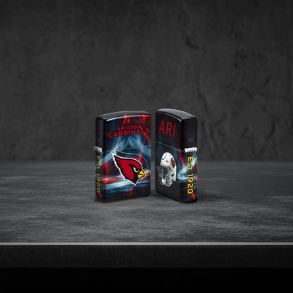 Lifestyle image of two Zippo NFL Arizona Cardinals 540 Matte Windproof Lighters, one showing the front of the lighter and the other showing the back, standing on a dark grey surface.