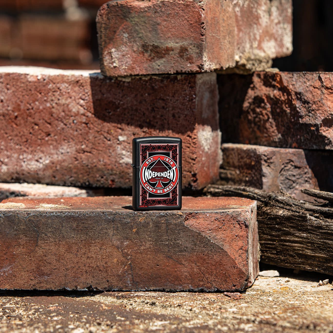 Lifestyle image of Zippo Independent Trucks Design Black Matte Windproof Lighter standing on a loose brick with more bricks surrounding.