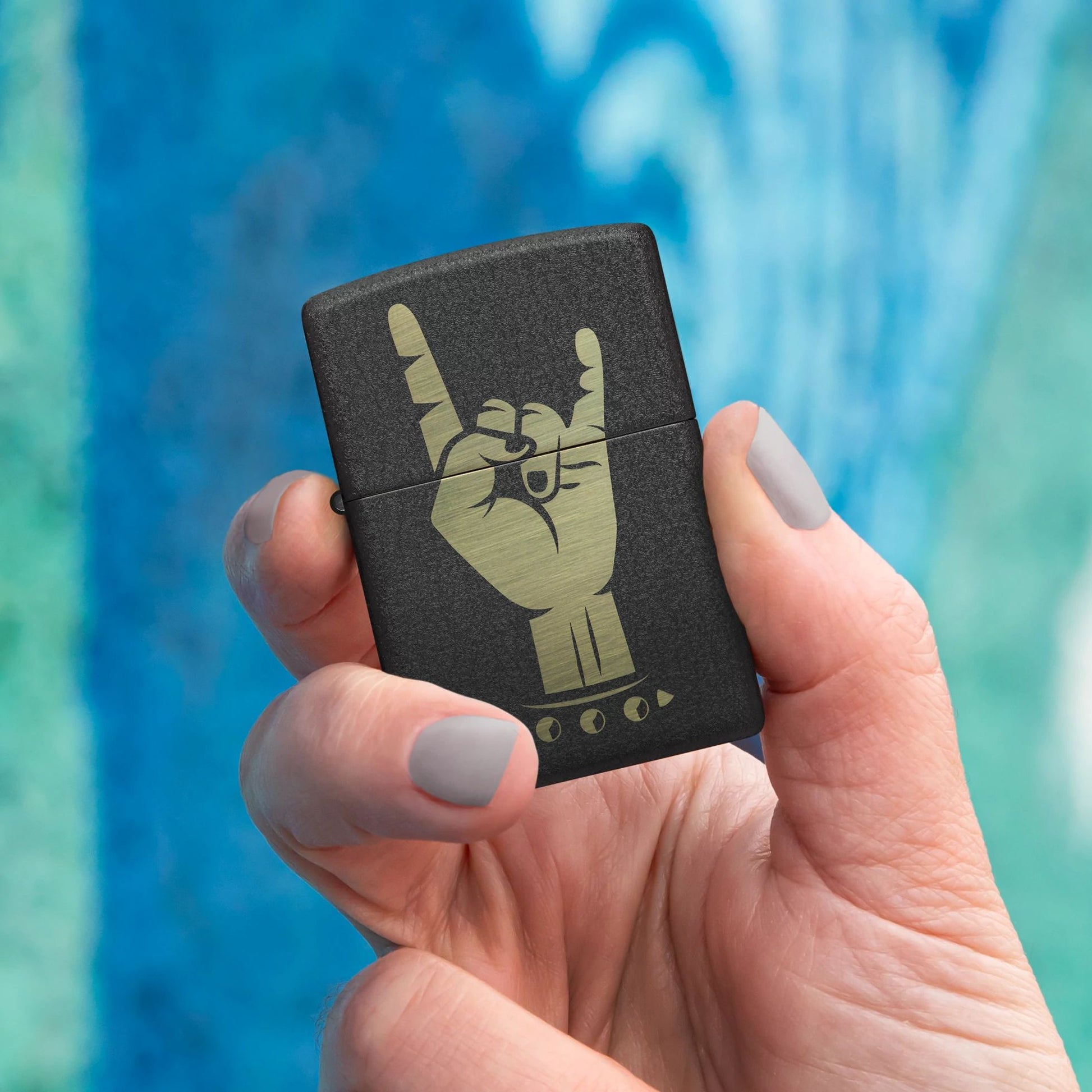 Lifestyle image of Zippo Rock On Design Black Crackle® Windproof Lighter being held in hand while showing the front of the lighter with a blue and green graffiti background. 

