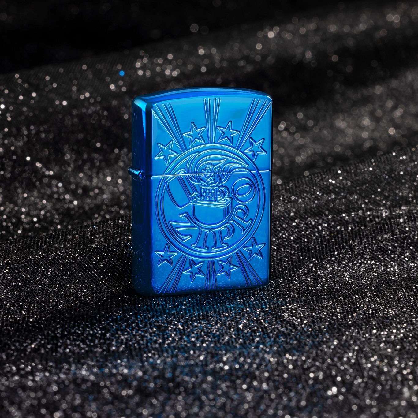 Lifestyle image of Zippo Starburst Design Armor® High Polish Blue Windproof Lighter standing with a black shimmer background.

