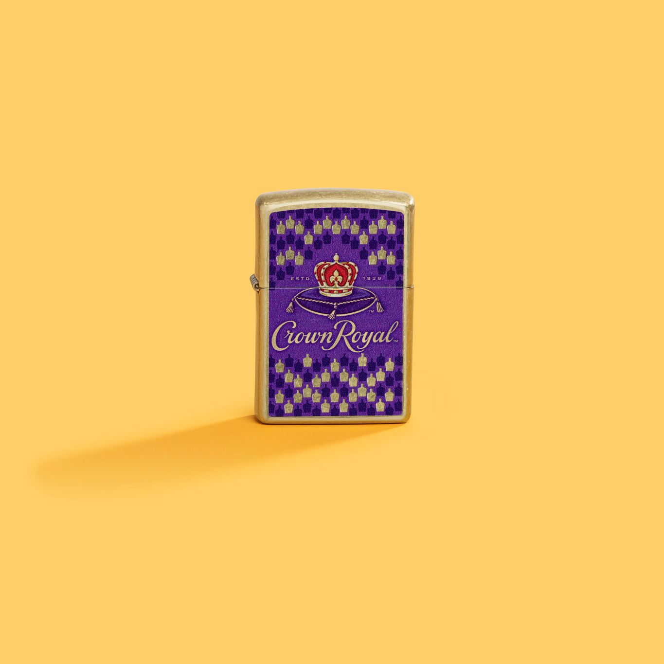 Lifestyle image of Zippo Crown Royal® Bottle Design Street Brass Windproof Lighter showing the front of the lighter with a yellow background.
