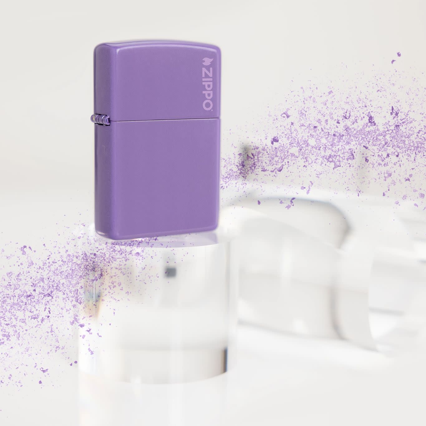 Lifestyle image of Zippo Classic Smoky Lavender Zippo Logo Windproof Lighter standing on a clear cylinder with a spray of purple on either end.