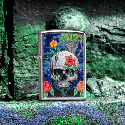 Lifestyle image of Zippo Skull Sprout Design Street Chrome Windproof Lighter standing on a ledge of a graffiti-covered surface showing the front of the lighter. 

