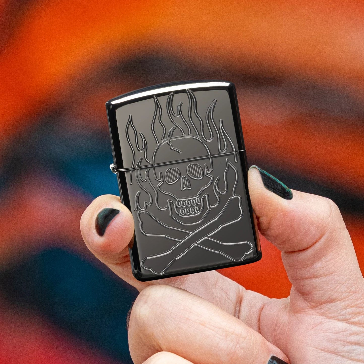 Lifestyle image of Zippo Flaming Skull Design Armor® High Polish Black Windproof Lighter being held in hand while showing the front of the lighter with an orange and black graffiti background. 

