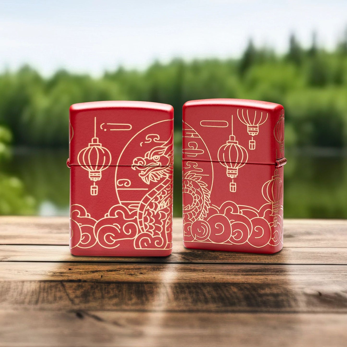 Lifestyle image of two Zippo Chinese New Year Design Red Matte Windproof Lighters standing on a wooden railing with a creek and green trees as the background; one showing the front of the lighter, while the other is showing the back of the lighter. 