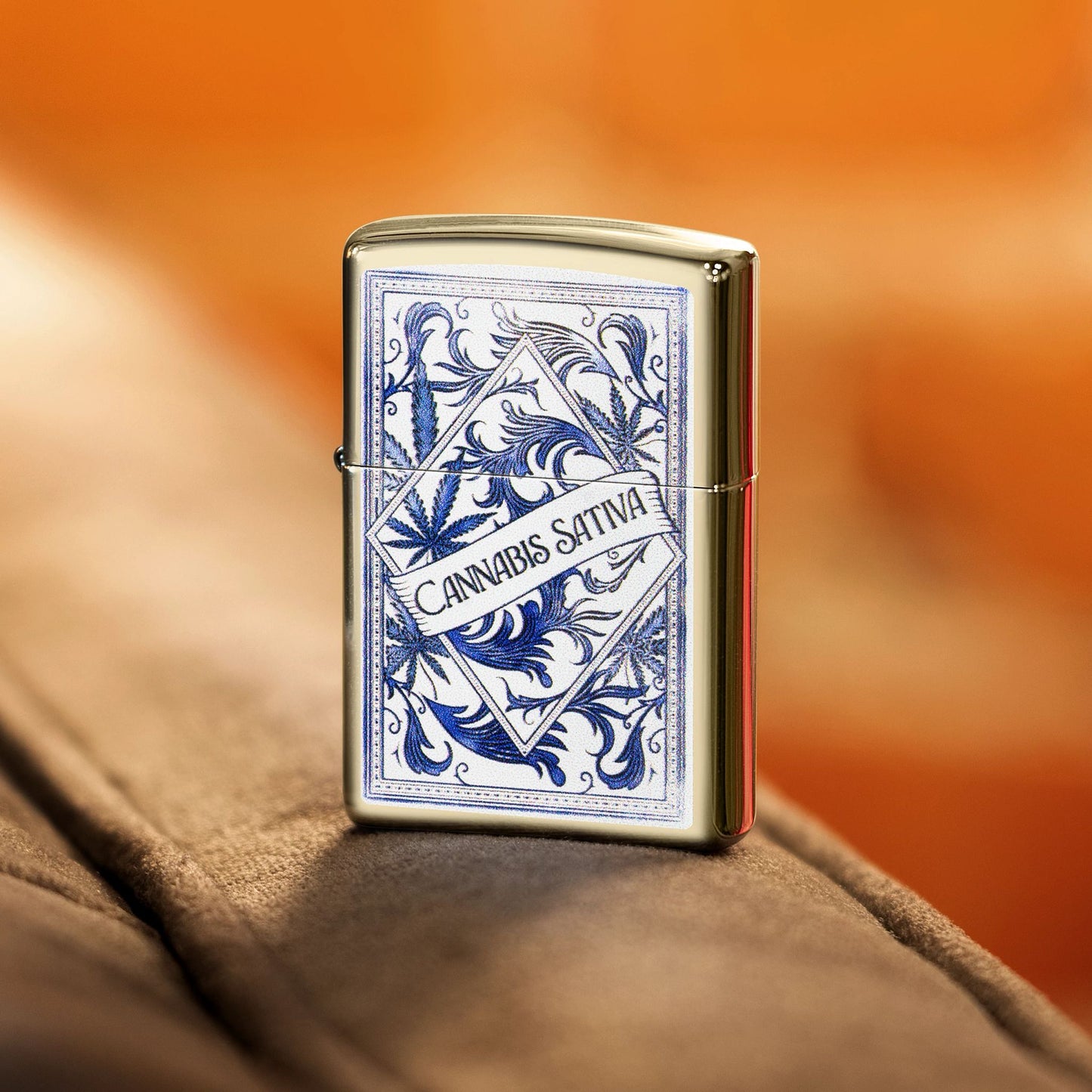 Lifestyle image of Zippo Sativa Serenity Design Champagne Windproof Lighter standing on the armrest of a tan couch showing the front of the lighter. 

