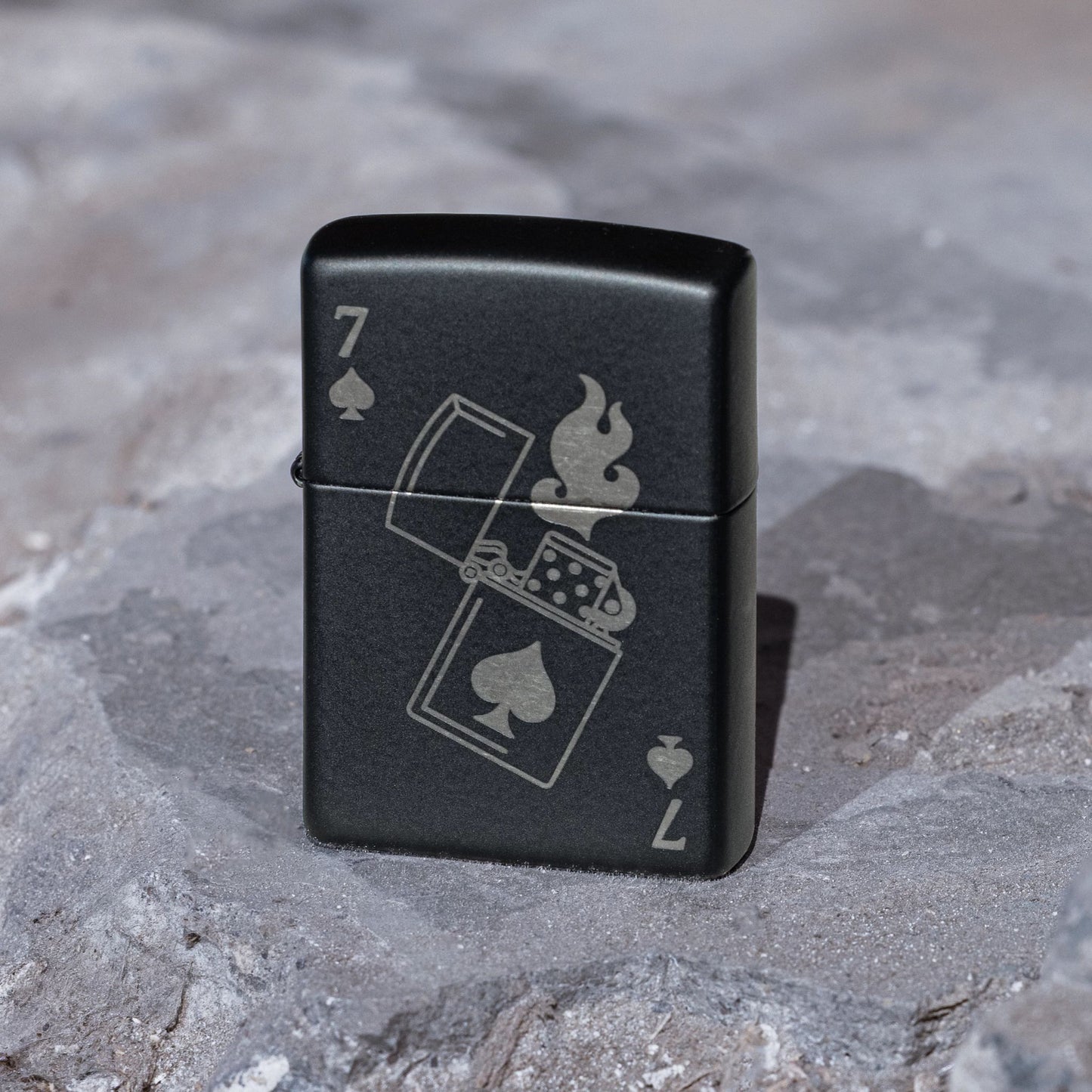 Lifestyle image of Zippo Lucky 7 Design Black Matte With Chrome Windproof Lighter standing on a stone surface showing the front of the lighter. 

