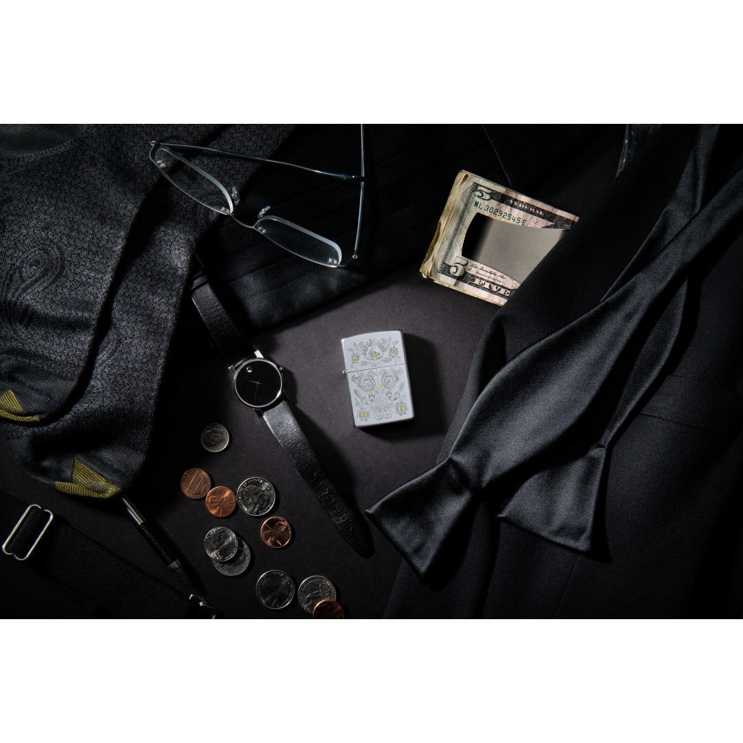 Lifestyle image of Painted Floral Satin Chrome Windproof Lighter laying with items such as money, a watch, ties, glasses, and coins.