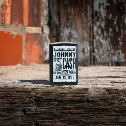 Lifestyle image of Zippo Johnny Cash Folsom State Prison Poster Design Black Matte Windproof Lighter standing on a piece of wood with a brick background.