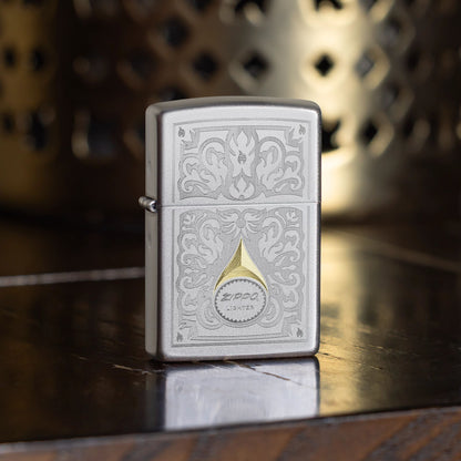 Lifestyle image of Zippo Vintage Filigree Design Satin Chrome Windproof Lighter standing on a dark wooden table showing the front of the lighter with a decorative metal candle holder as the background. 

