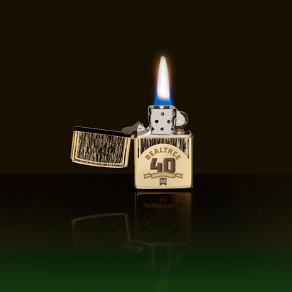 Lifestyle image of Zippo Realtree® 40th Anniversary Design Champagne Windproof Lighter showing the front of the lighter with its lid open and lit with a black and green ombre background. 

