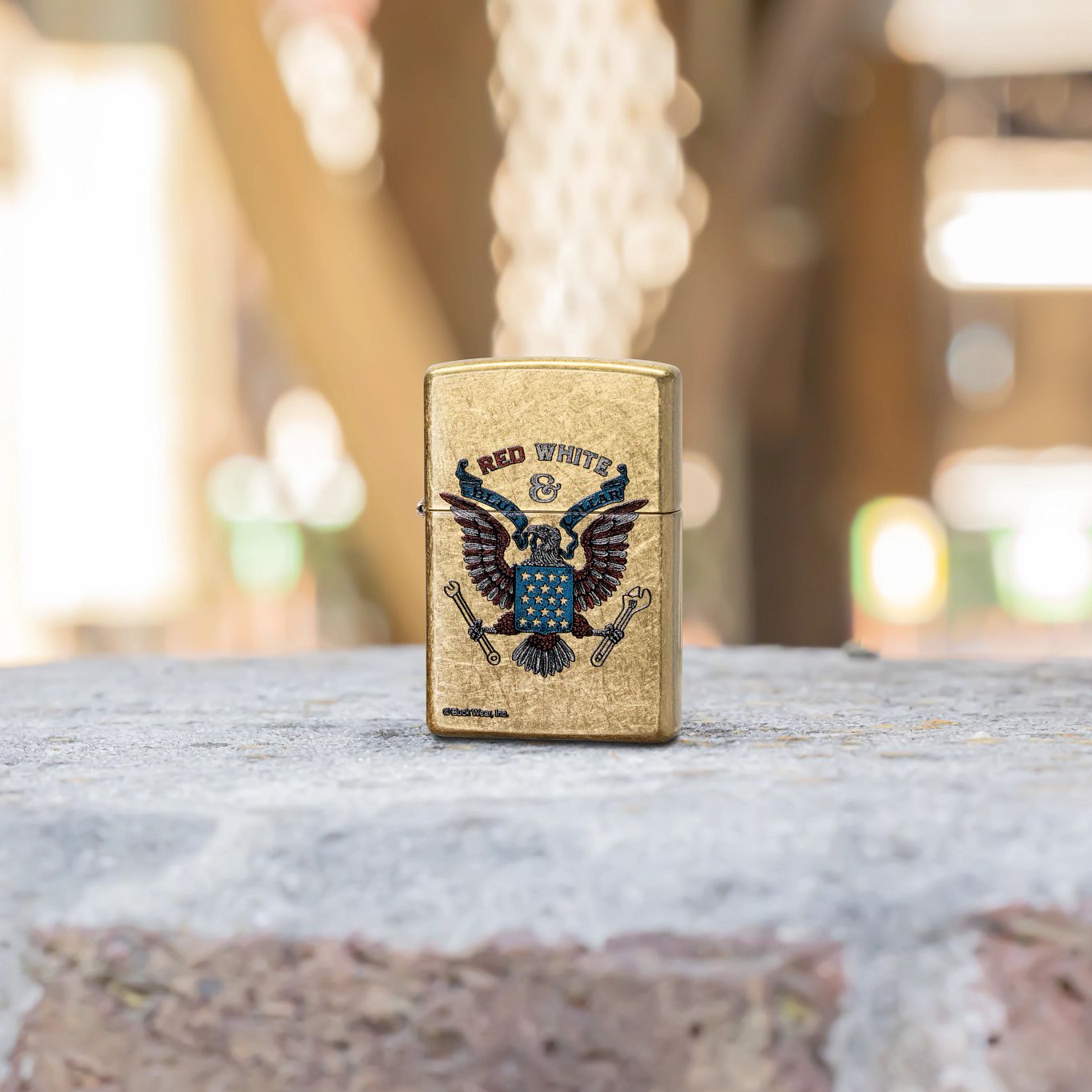 Lifestyle image of Zippo Buck Wear™ Red White & Blue Collar Design Street Brass Windproof Lighter standing on a brick wall showing the front of the lighter. 

