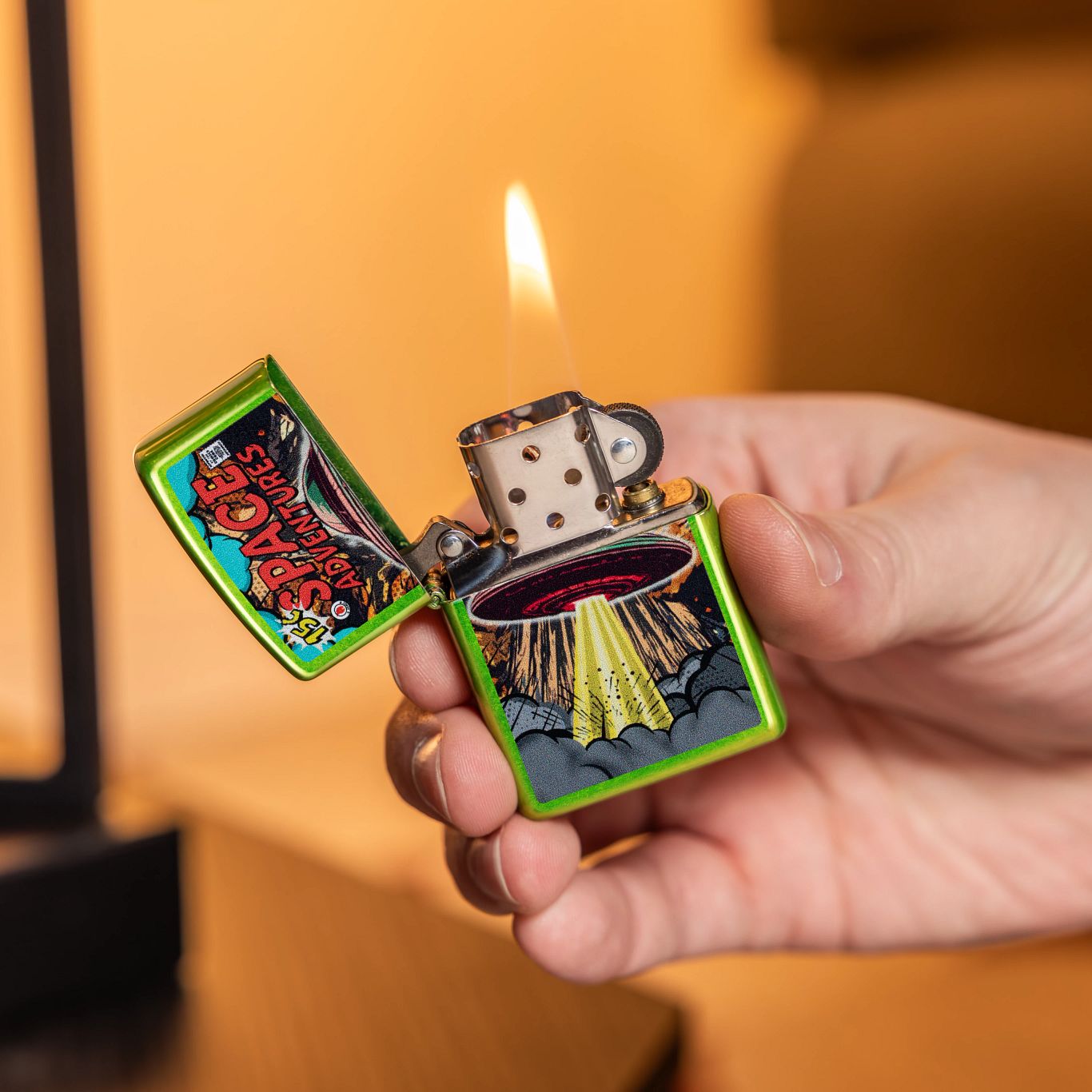 Lifestyle image of Zippo Space Adventures Design Classic Lurid Windproof Lighter lit in hand in front of a dark yellow background.