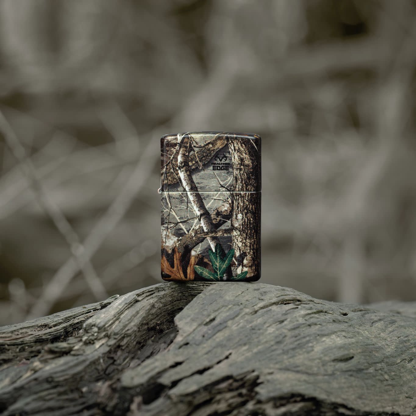 Lifestyle image of Zippo Realtree® EDGE™ Camo Design 540 Matte Windproof Lighter standing on a fallen limb in a wooded scene.