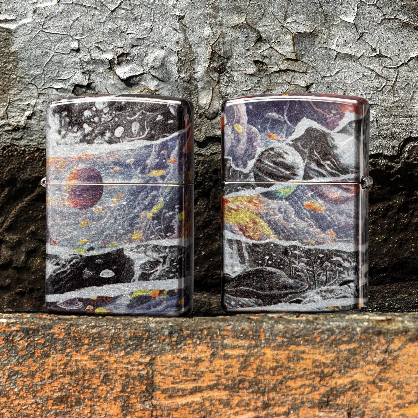 Lifestyle image of two Zippo Fusion Galaxy Design 540 Tumbled Chrome Windproof Lighters standing on painted concrete that is peeling; one showing the front of the lighter, while the other is showing the back of the lighter. 

