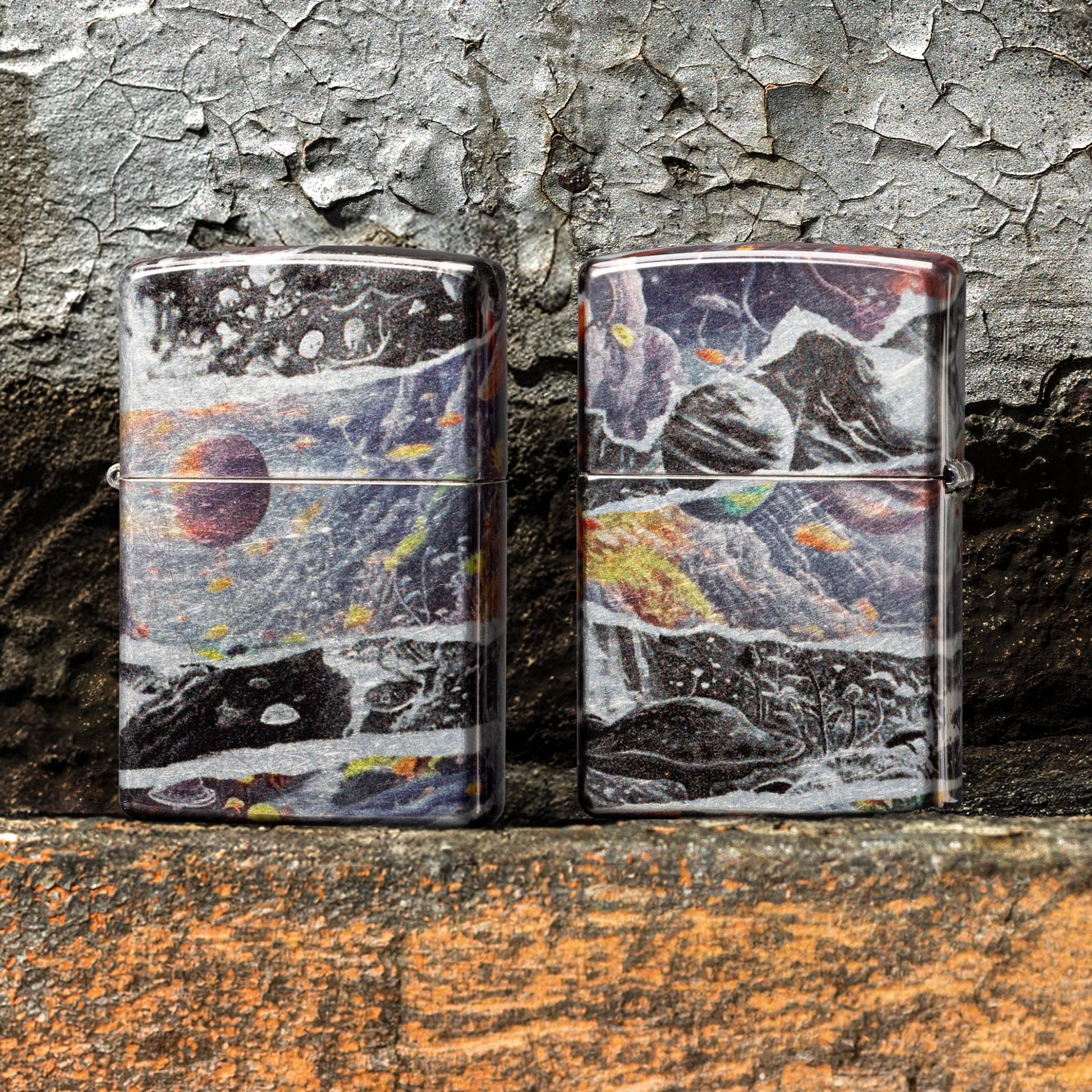 Lifestyle image of two Zippo Fusion Galaxy Design 540 Tumbled Chrome Windproof Lighters standing on painted concrete that is peeling; one showing the front of the lighter, while the other is showing the back of the lighter. 

