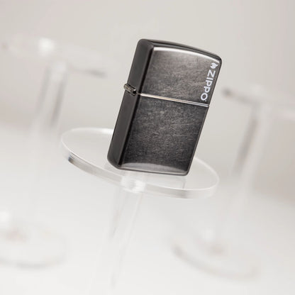 Tilted lifestyle image of Zippo Classic Grey Zippo Logo Windproof Lighter standing on the first of three clear pedestals, with the other two in the background.