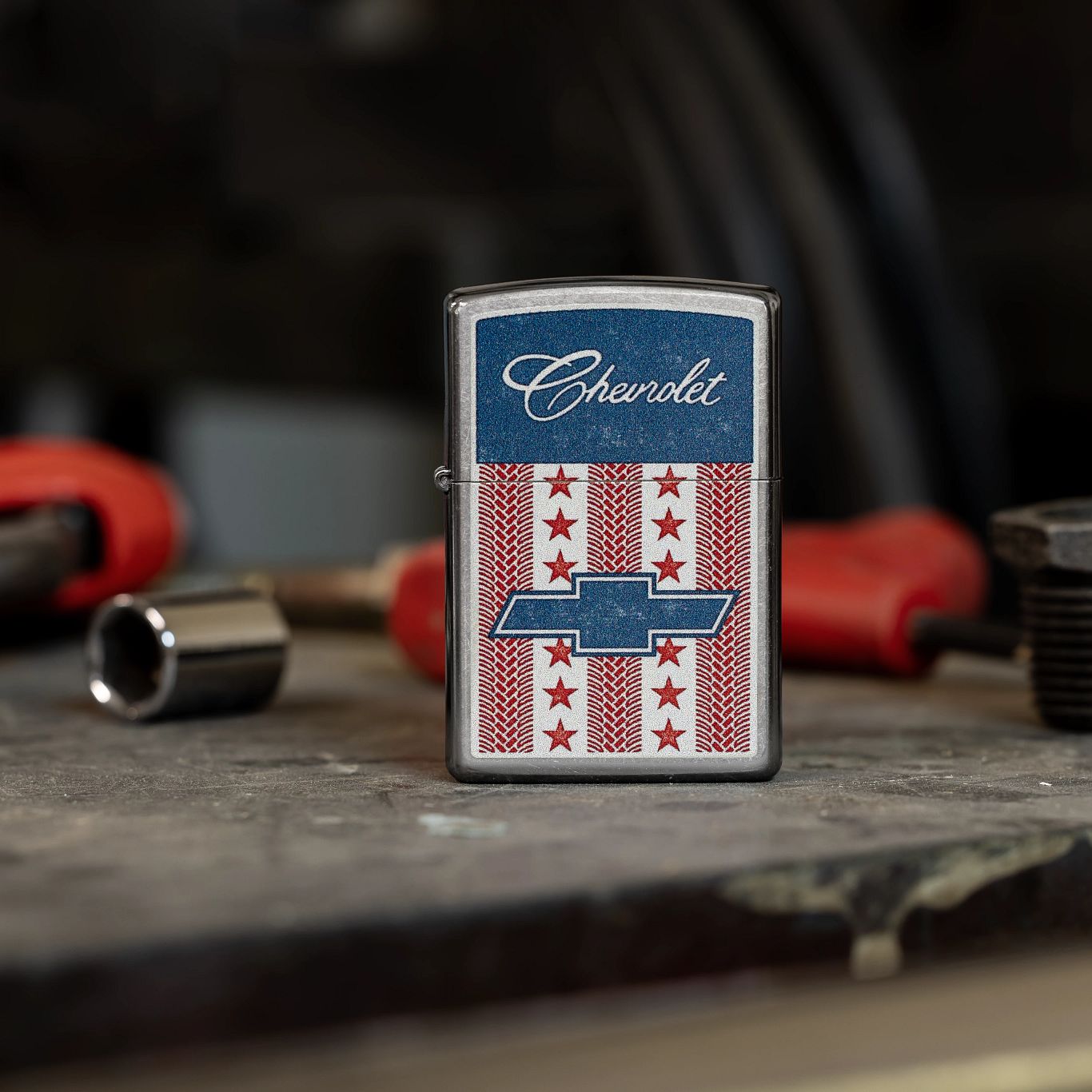 Lifestyle image of Zippo Chevrolet® Stars and Stripes Design Street Chrome Windproof Lighter standing on a workbench with automotive tools.

