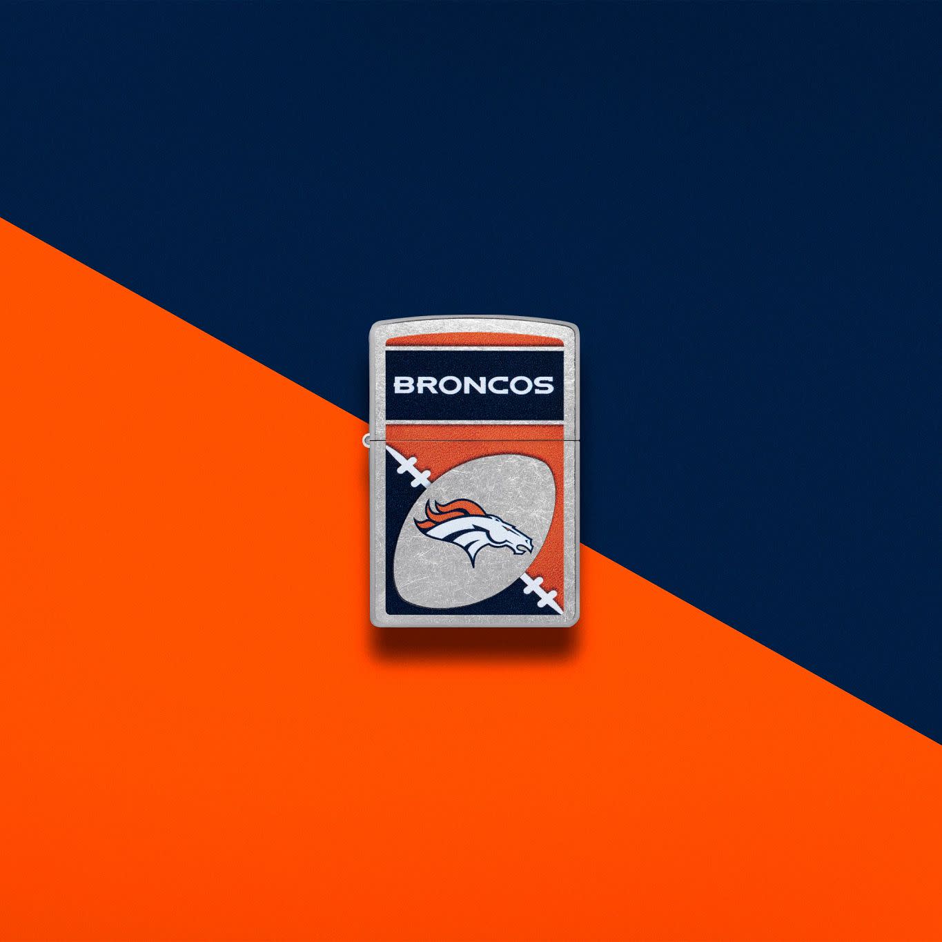 Lifestyle image of Zippo NFL Denver Broncos Street Chrome Windproof Lighter set on an orange and navy background.