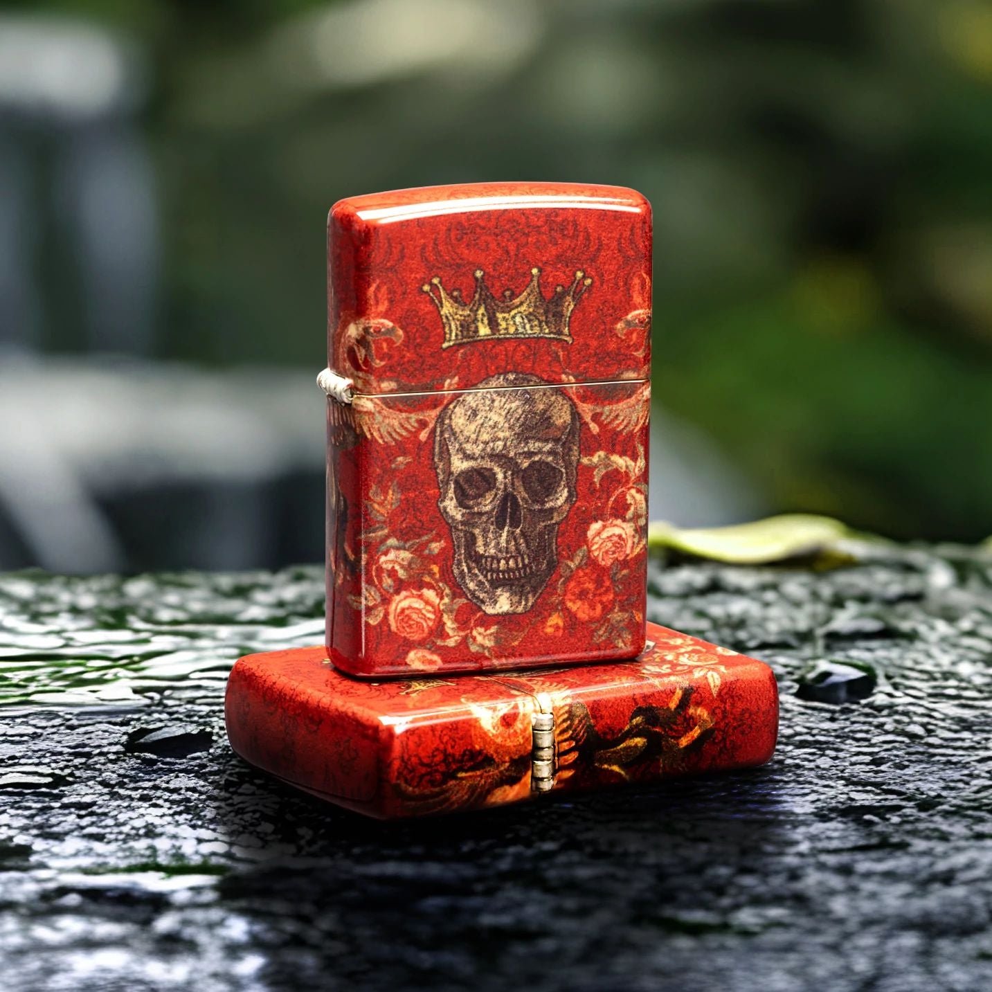 Lifestyle image of two Zippo Skull Heraldry Design Tumbled Brass Windproof Lighters; one lying flat on a wet rocky surface showing the top of the lid and hinge side of the lighter, while the other lighter is standing on top of the lighter that is lying flat showing the front of the lighter with a blurred small  waterfall and greenery as the background. 