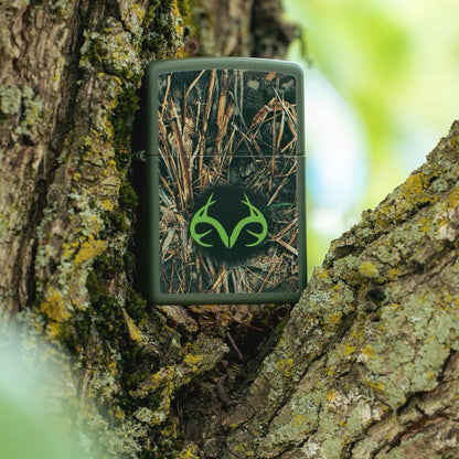 Lifestyle image of Zippo Realtree® Brush Design Green Matte Windproof Lighter standing on the branch bark ridge of a tree showing the front of the lighter. 


