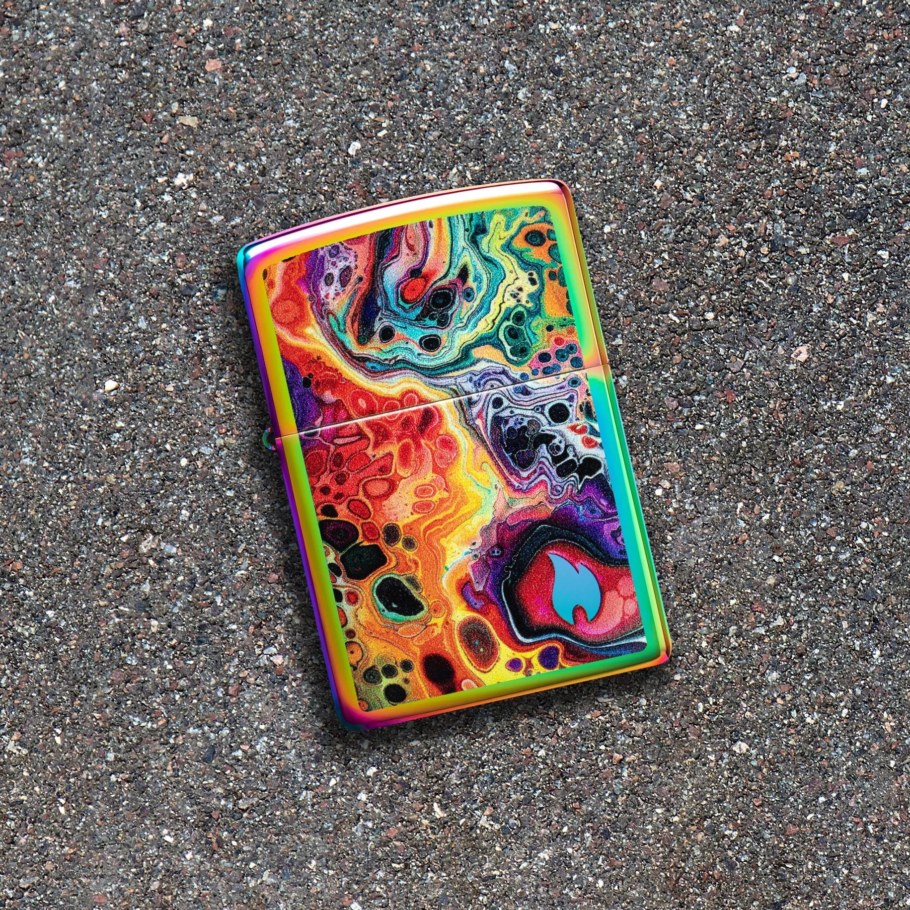 Lifestyle image of Zippo Mesmerizing Magma Design Multi-Color Windproof Lighter lying on a blacktop surface while showing the front of the lighter. 

