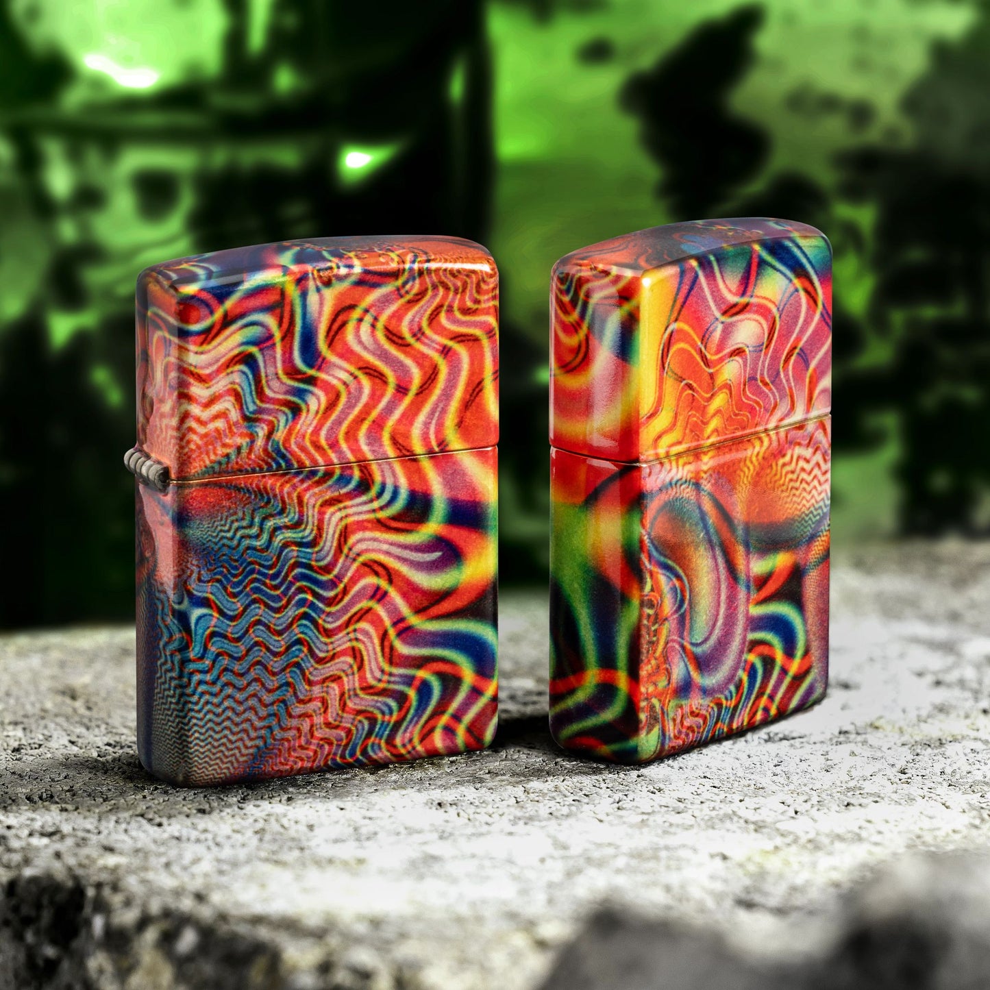 Lifestyle image of two Zippo Fusion Waves Design 540 Tumbled Brass Windproof Lighters standing on a rock; one showing the front and hinge side of the lighter while the other shows the back and non-hinge side of the lighter with a green background. 

