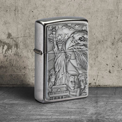 Lifestyle image of Zippo American Icons Emblem Street Chrome Windproof Lighter standing on a concrete floor showing the front and hinge side of the lighter. The background is a concrete wall. 

