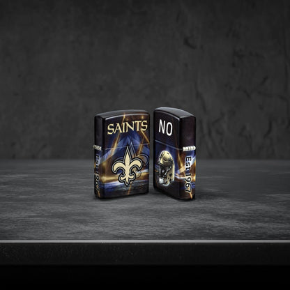 Lifestyle image of two Zippo NFL New Orleans Saints 540 Matte Windproof Lighters, one showing the front of the lighter and the other showing the back, standing on a dark grey surface.