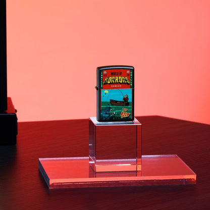 Lifestyle image of Zippo In Deep Trouble Design Black Matte Windproof Lighter standing on a clear stand on a table showing the front of the lighter with a pink/red background. 


