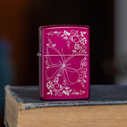 Lifestyle image of Zippo Butterfly Bliss Design Candy Raspberry Windproof Lighter standing on the cover of a book showing the front of the lighter. 

