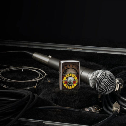 Lifestyle image of Zippo Guns N' Roses Logo Design Street Chrome Windproof Lighter standing next to a microphone and cables, while showing the front of the lighter. 

