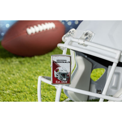 Lifestyle image of Zippo NFL Arizona Cardinals Helmet Design Street Chrome Windproof Lighter standing on the facemask of a white helmet showing the front of the lighter with a football lying on a football field as the background.


