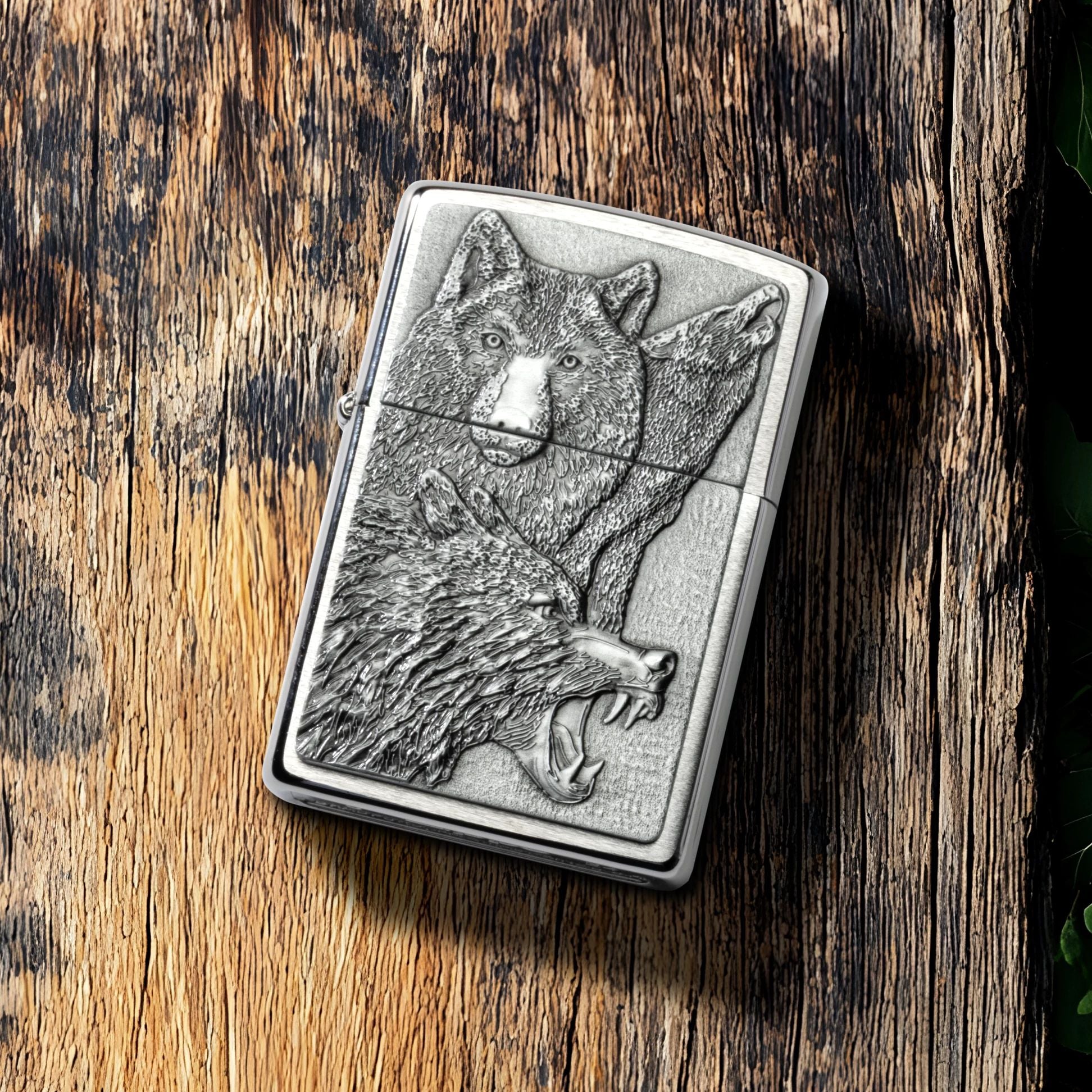Lifestyle image of Zippo Wolf Pack Emblem Brushed Chrome Windproof Lighter lying on a plank of old weathered wood, showing the front of the lighter. 

