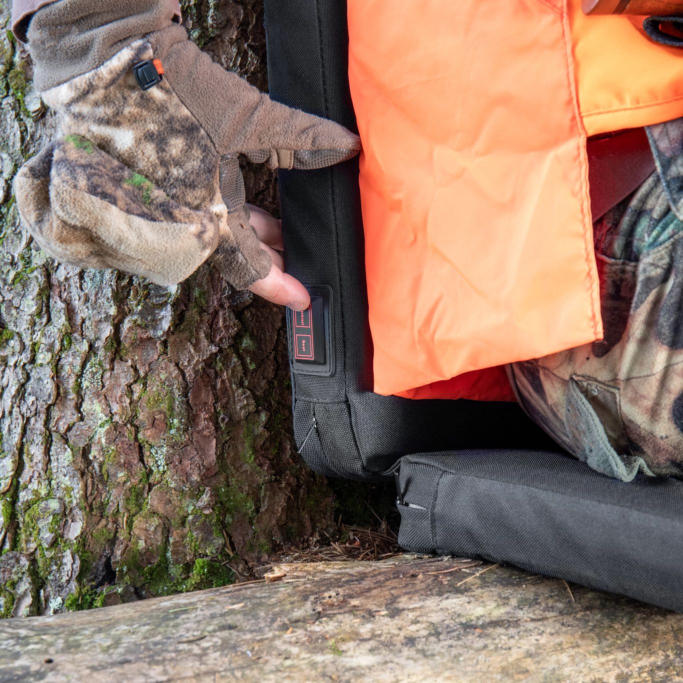 Lifestyle image of Zippo Heated Seat - Double showing a hunter sitting on a tree trunk using the heated seat. 