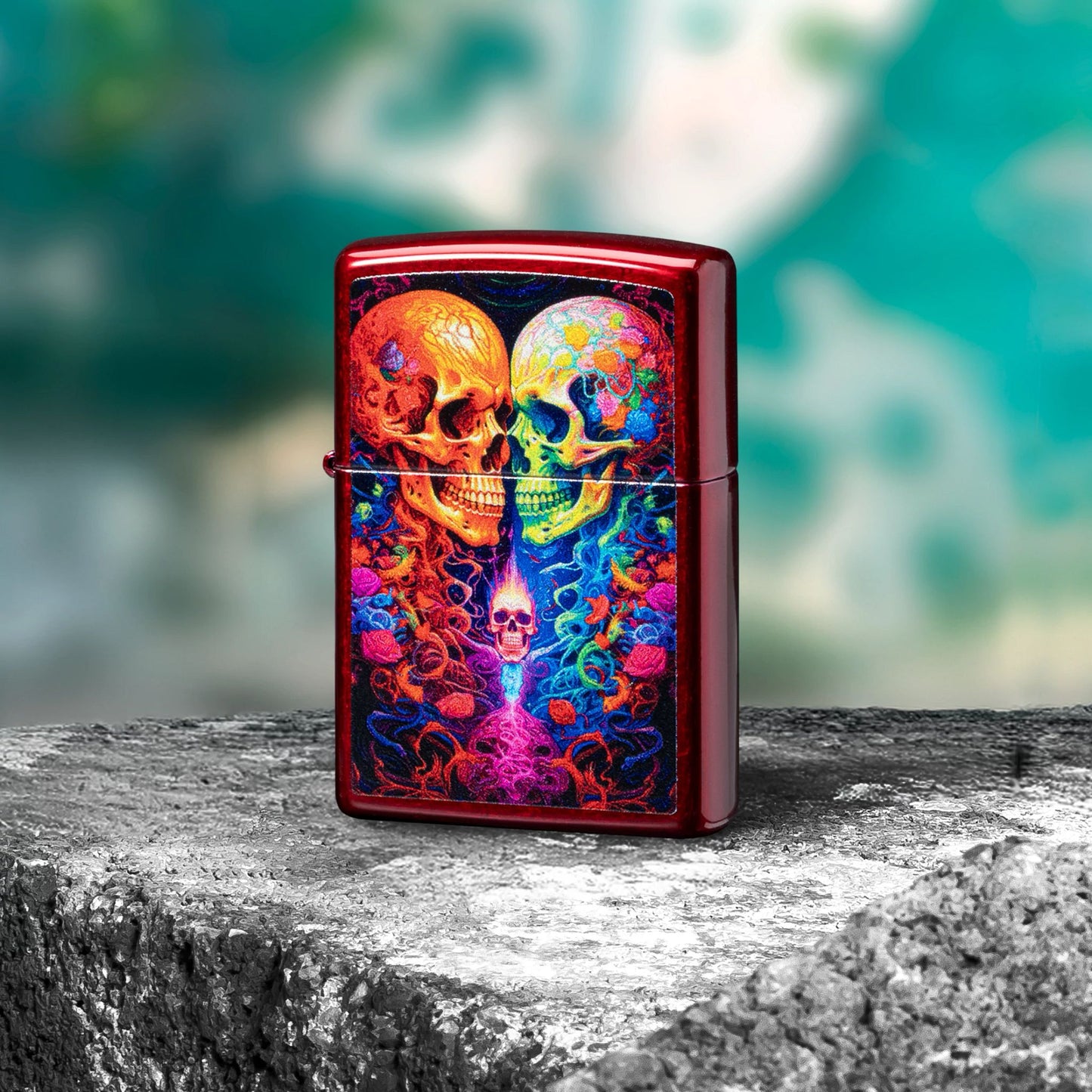 Lifestyle image of Zippo Candy Skulls Design Candy Apple Red Windproof Lighter standing on a rock showing the front of the lighter with bluish green graffiti as the background.  

